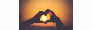 a hands making a heart shape with the sun in the background